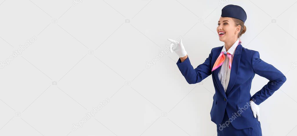 Beautiful stewardess pointing at something on light background with space for text