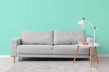 Masası ve lambası olan şık gri kanepe nane duvarının yanında.