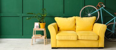 Sarı kanepe, bisiklet ve merdiven. Yeşil duvarın yanında ev bitkisi ve metin için yeri var.