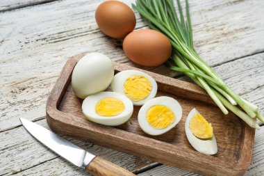 Kaynamış tavuk yumurtası ve hafif ahşap arka planda yeşil soğanlı pano.