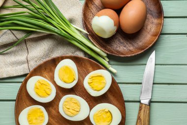 Haşlanmış tavuk yumurtası, yeşil soğan ve ahşap arka planda bıçak tabakları ile kompozisyon