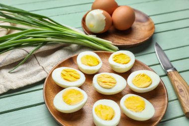 Haşlanmış tavuk yumurtası ve ahşap kaplama yeşil soğan tabakları, yakın plan.