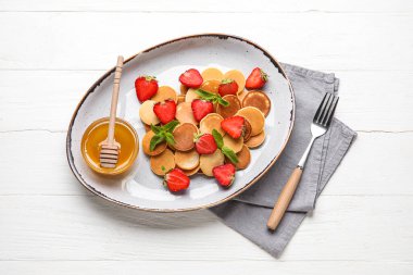 Mini krep, çilek ve arka planda bir kase bal.