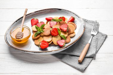 Mini krep, çilek ve arka planda bir kase bal.