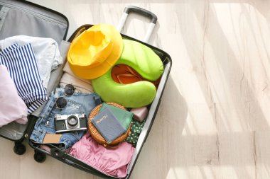 Opened suitcase with clothes and different accessories for travelling on light wooden floor clipart