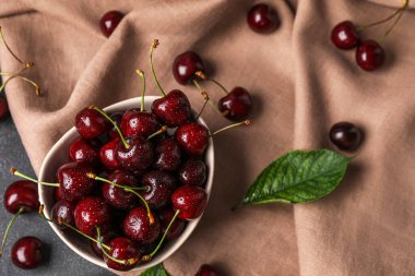 Olgun kirazlı kase ve kumaş arkaplanda su damlaları