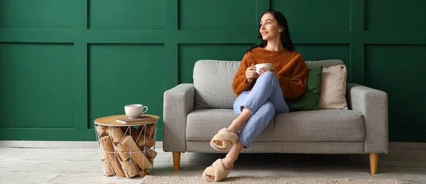 Happy young woman with cup of tea resting on couch at home