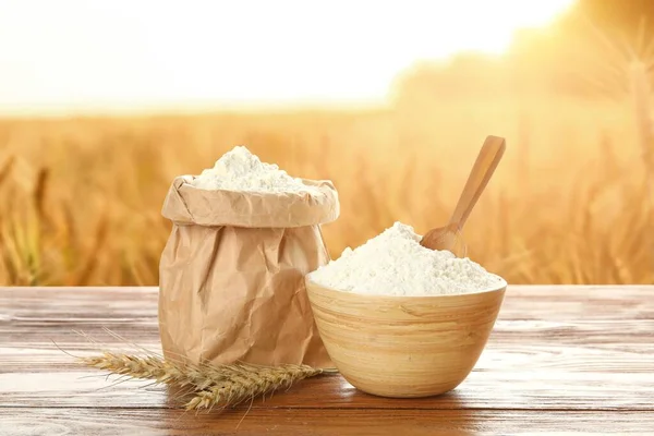 Bowl and paper bag with wheat flour on wooden table in field