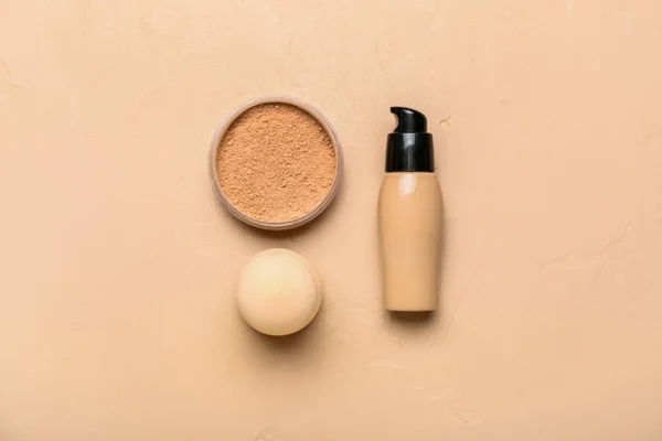 Bottle of makeup foundation, powder and sponge on color background