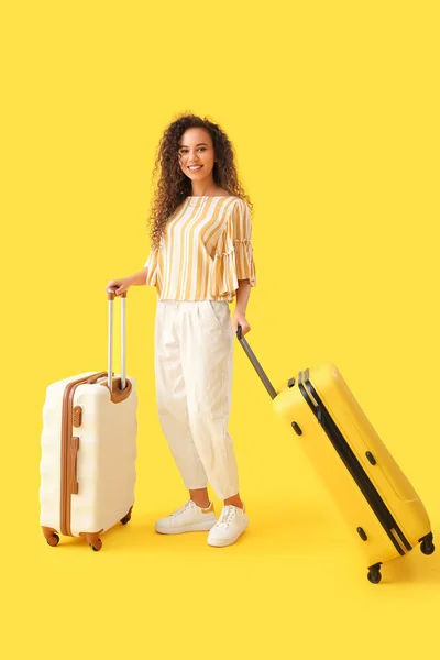 Young African-American woman with suitcases on yellow background