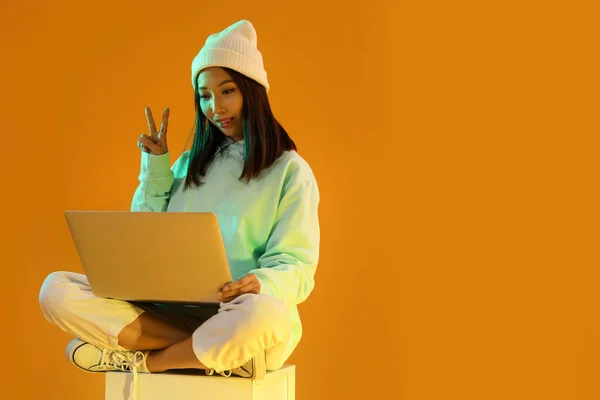 Female Asian blogger with laptop on orange background