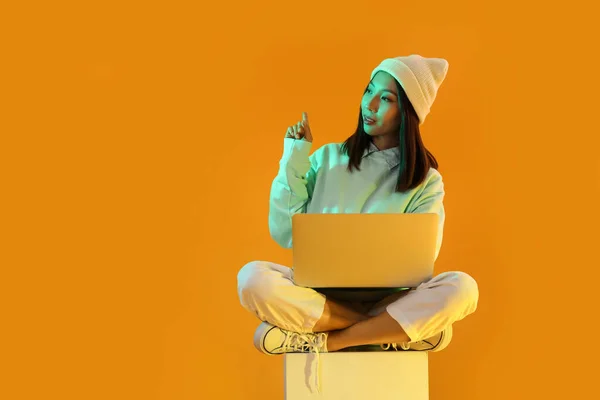 Female Asian blogger with laptop on orange background