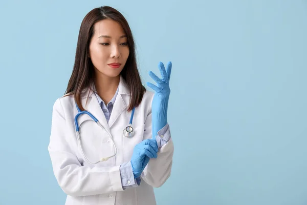 Female Asian Doctor Putting Rubber Gloves Blue Background — Stockfoto