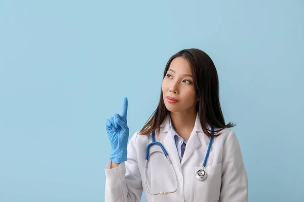 Female Asian doctor pointing at something on blue background