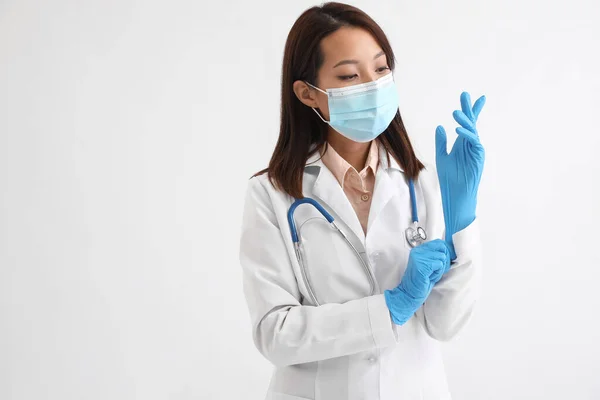 Female Asian doctor putting on rubber gloves against white background
