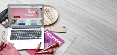 Diz üstü bilgisayarda güzellik blogu, dergi, dekoratif kozmetik ürünler ve hafif ahşap zeminde metin için yeri olan aksesuarlar.