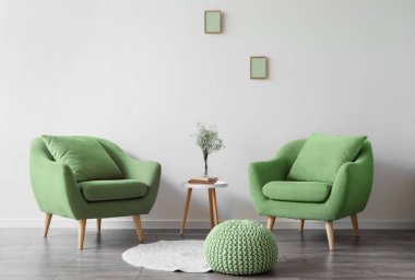 Modern oturma odasının içinde yeşil koltuklar, masa ve ışık duvarının yanında puf.