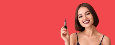 Kırmızı arkaplanda ruj tutan güzel, gülümseyen bir kadın.