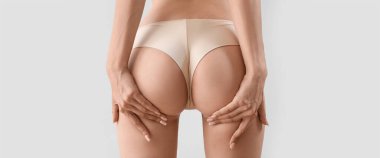 Buttocks of young woman in underwear on light background