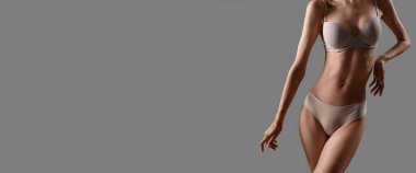 İç çamaşırlı, gri arka planda, mesaj için yeri olan zayıf genç bir kadın.