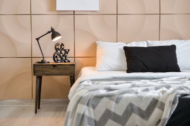 Yatak odasındaki bej duvarın yanında parlayan lamba ve dekor olan masa.