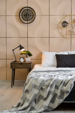 Table with lamp, alarm clock and bonsai near beige wall in bedroom