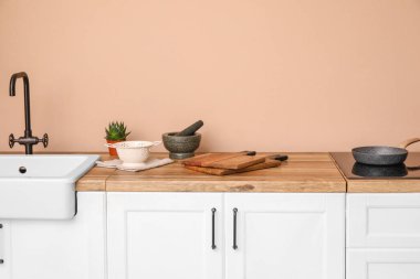 Tahta kesmek, topuzlu havan ve bej duvarın yanındaki tezgahta kevgir.