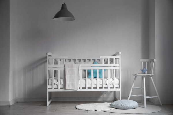 Интерьер детской комнаты с удобной кроваткой и стулом возле белой стены