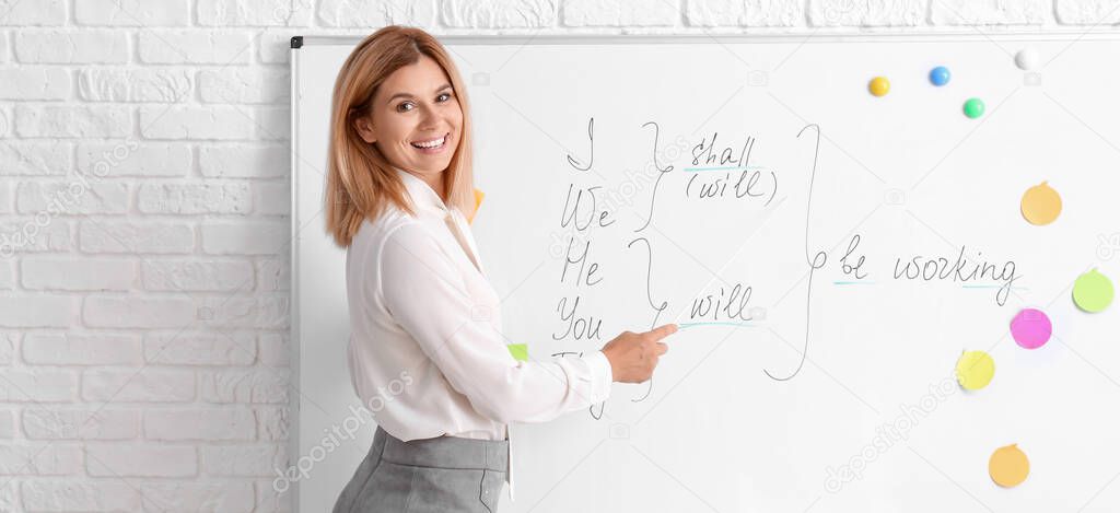 Beautiful English teacher near blackboard in classroom