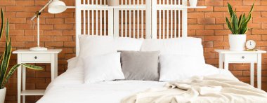 Temiz çarşafları ve tuğla duvarın yanındaki masaları olan rahat bir yatak.