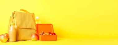 Child's bag and lunchbox with tasty food on yellow background with space for text