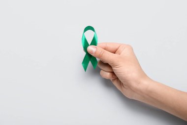 Hand with green ribbon on light background. Liver cancer concept