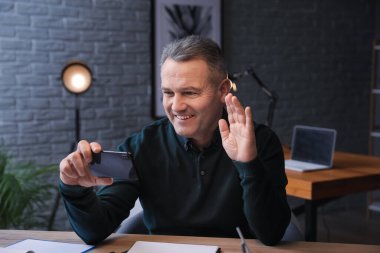 Happy mature man with mobile phone video chatting late in evening