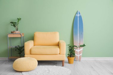 Sörf tahtası, puf, masa ve yeşil duvarlı rahat bir koltuk.