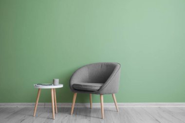 Comfortable armchair with table near green wall in room