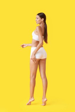 Young tanned woman in underwear on yellow background