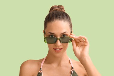Yeşil arka planda güneş gözlüklü, bronzlaşmış genç bir kadın, yakın plan.