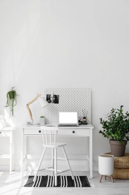 Workplace with laptop, lamp and pegboard near light wall