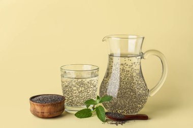 Renk zemininde chia tohumları olan bir sürahi su ve kase.
