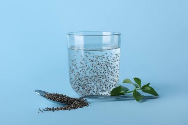 Renk zemininde chia tohumları olan bir bardak su ve kaşık