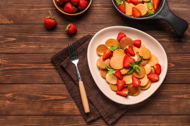 Minik krepli, çilekli ve ahşap zemin üzerinde nane yapraklı bir tabak.