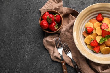 Koyu arkaplanda mini krep ve çilekli tabak, yakın plan.