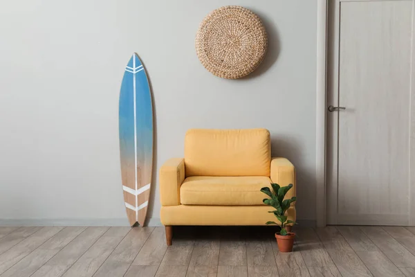 Comfortable armchair with surfboard and houseplant near light wall in room