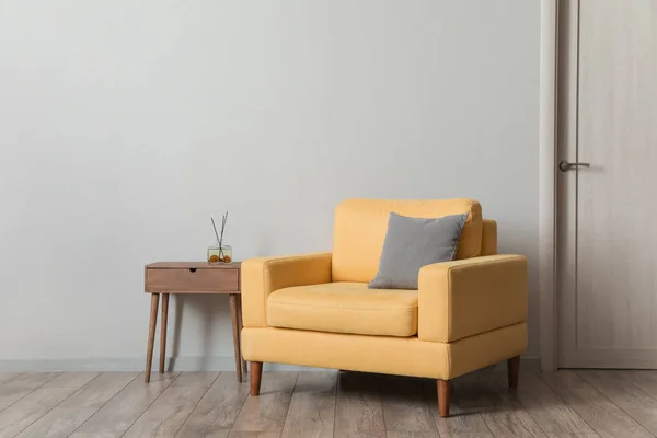 Comfortable armchair with table and air freshener near light wall in room