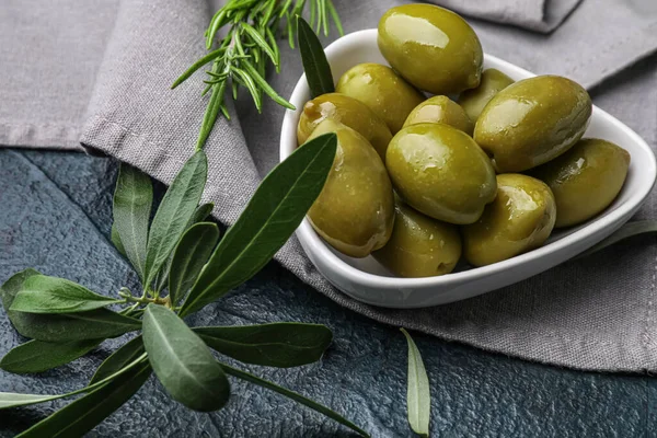 Bowl of tasty green olives and leaves on table, closeup
