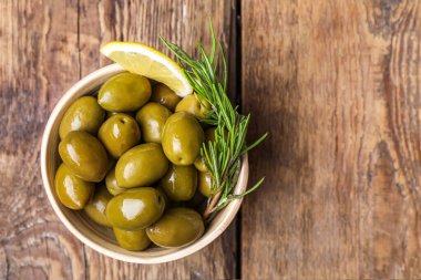 Limon dilimli ve ahşap kaplama biberiyeli bir kase lezzetli yeşil zeytin.