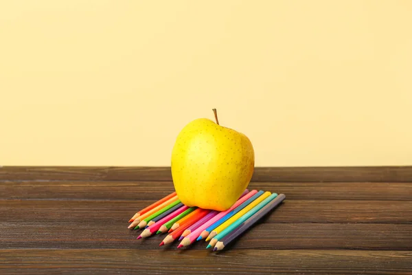 Apple with pencils on table against color background