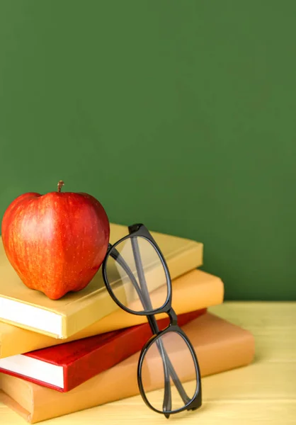 School books with apple and eyeglasses on table against green background