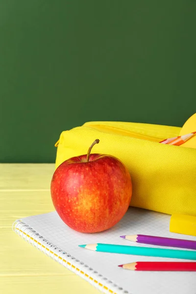 Pencil case with apple and notebook on table against green background