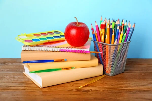 School stationery with apple and paints on table against blue background